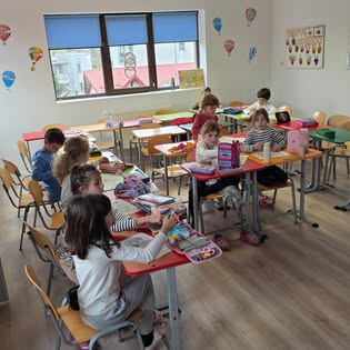 Copii lucrând împreună la mese, în sala luminoasă