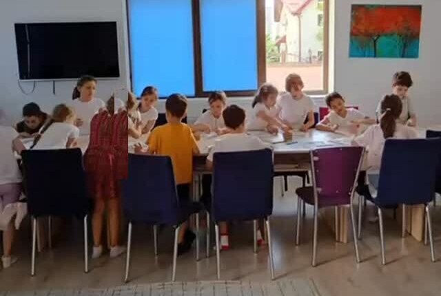 Copii la activități în jurul mesei mari, în sala luminoasă de la Educație Pozitivă